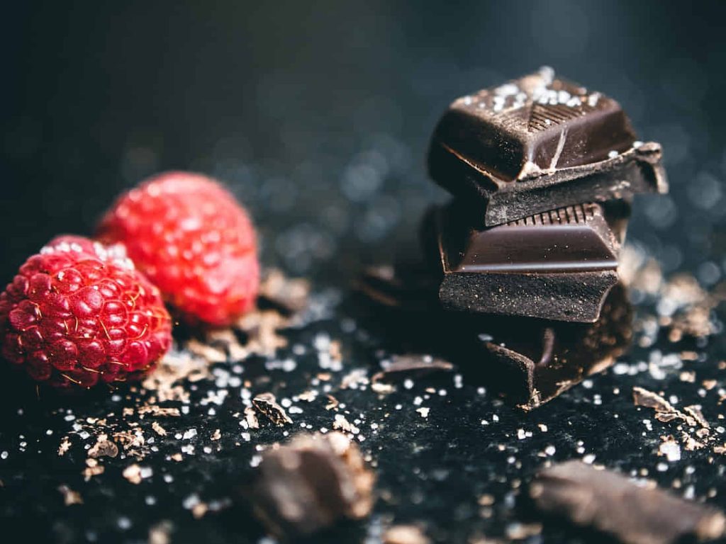 Close-Up Photo Of Stacked Chocolates Bars Beside Raspberries