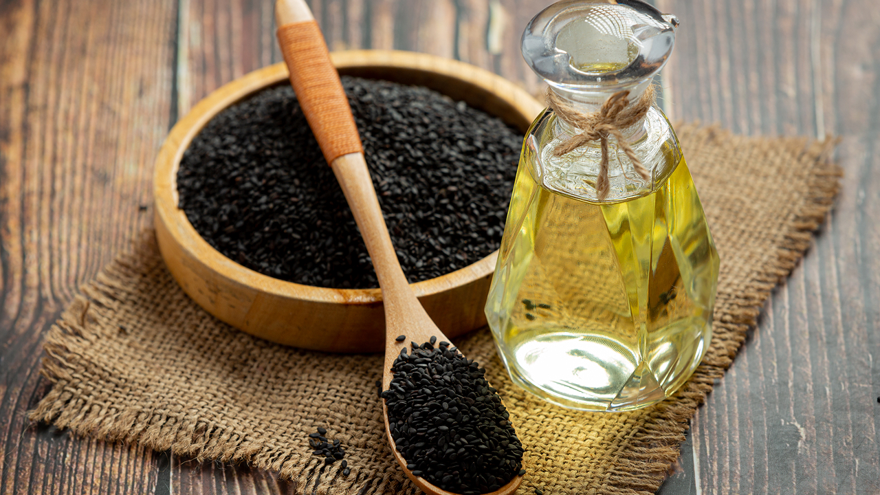 Black seed oil and raw black seeds on dark background