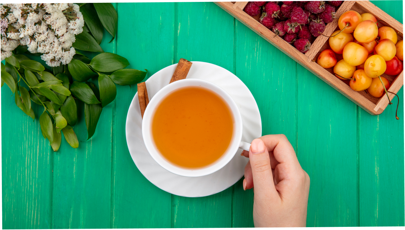 Top view of a woman hand holding a cup of tea with cinnamon and raspberries 