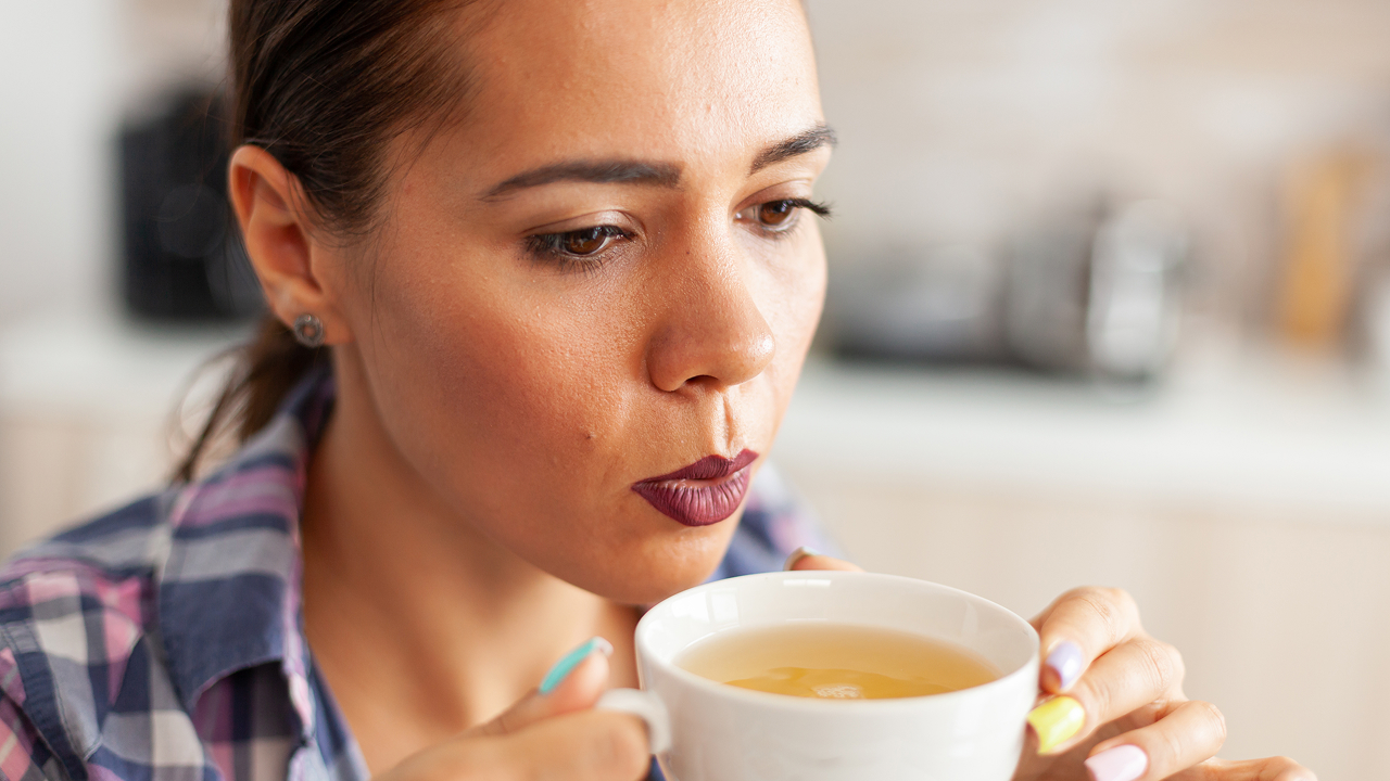 A close-up of a woman in the kitchen trying to drink green tea